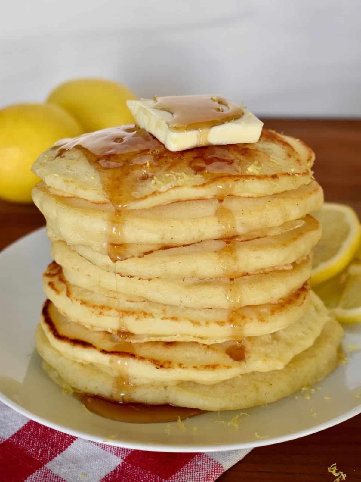 Stack of lemon ricotta pancakes with pancake mix on a white plate with a checkered napkin underneath. 