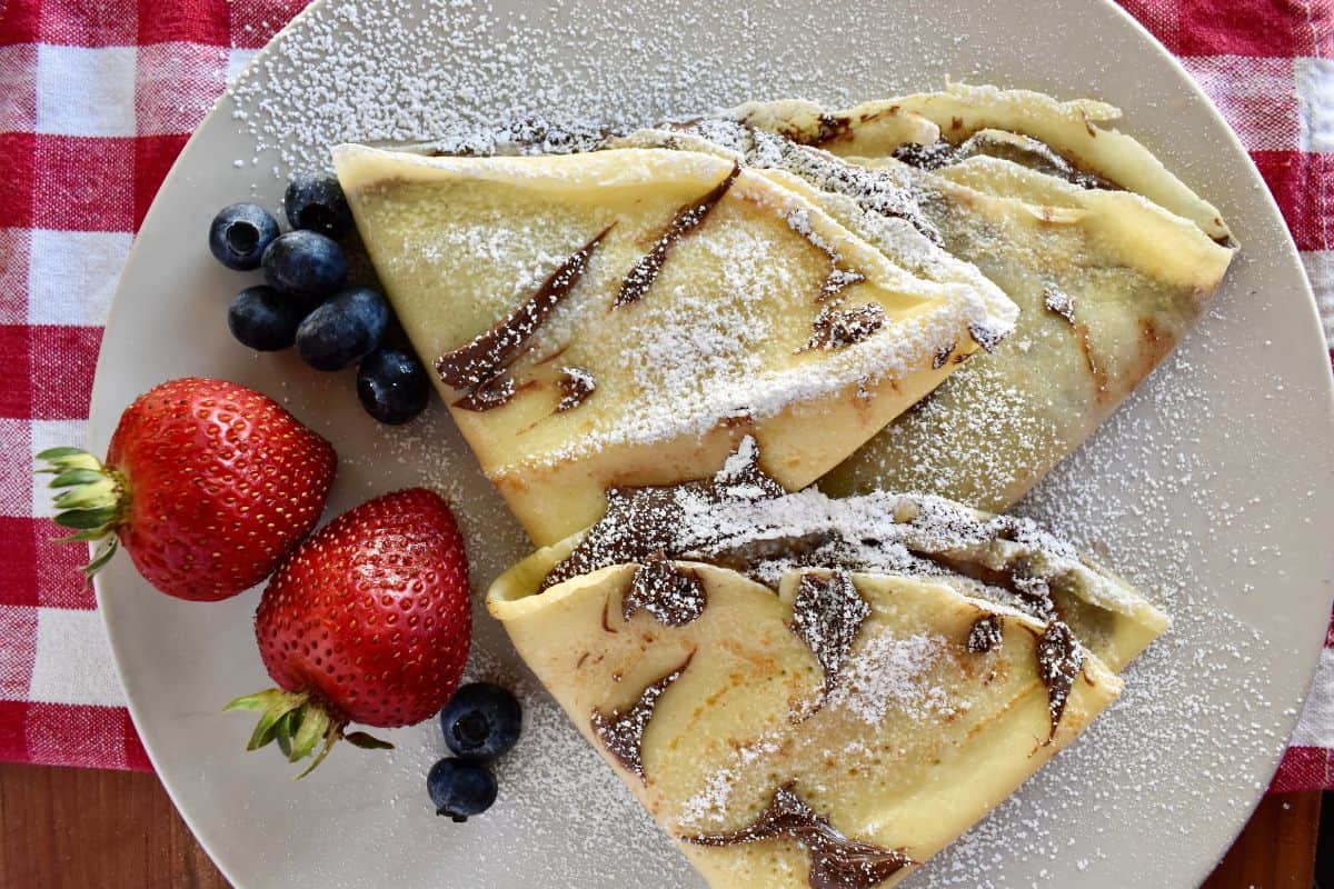 Overhead photo of Nutella crepes on a white plate with a checkered napkin underneath. 