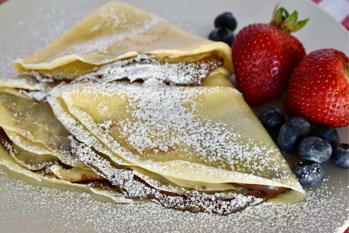 Nutella crepes folded and dusted with powdered sugar on a white plate. 