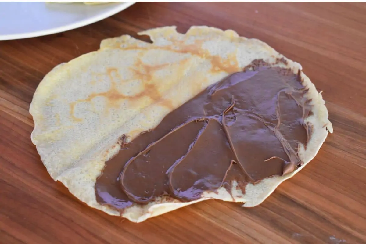 Thin pancake on a wood surface with Nutella spread over half of it. 