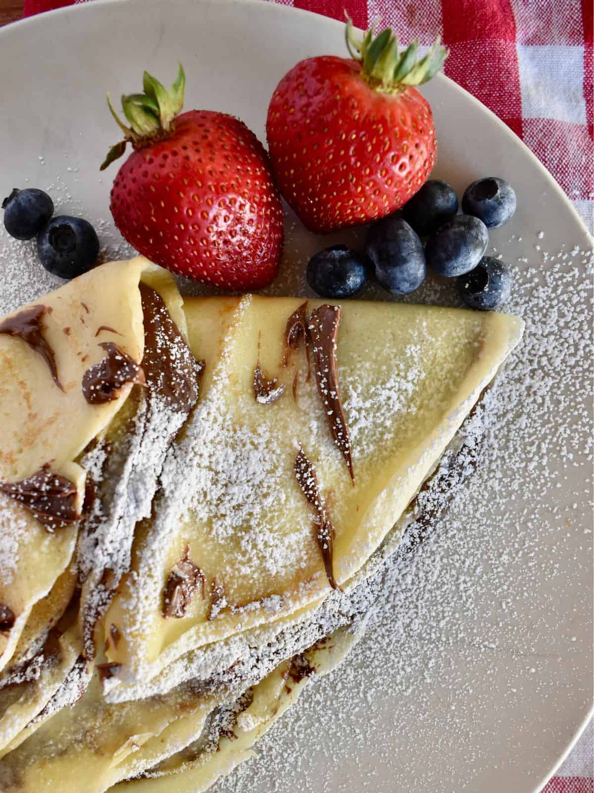 Nutella Crepes on a white plate with strawberries and blueberries. 