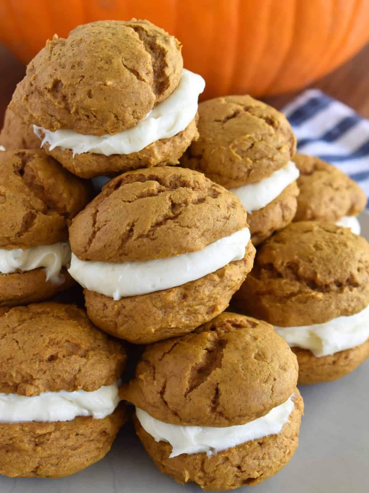 Pumpkin Whoopie Pies with Cake Mix stacked on a plate with a pumpkin in the background. 