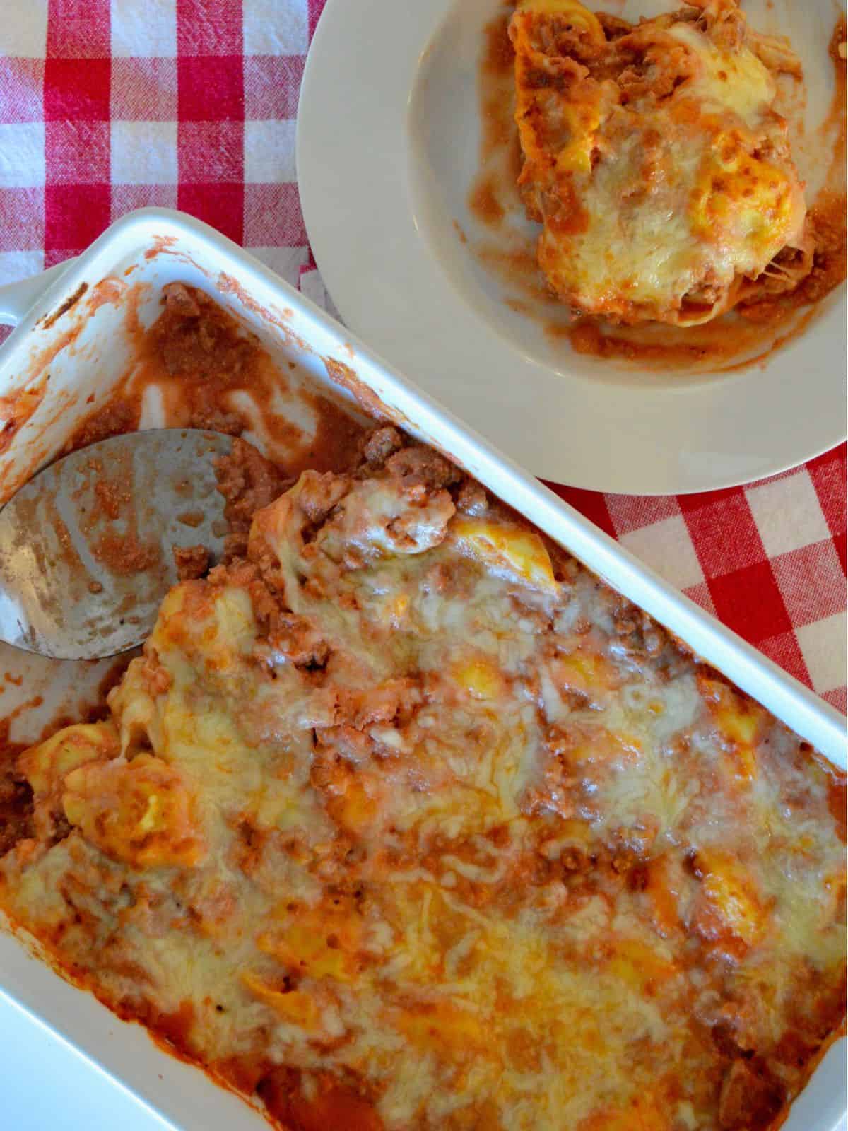 Overhead photo of baked tortellini casserole in a white casserole dish with a bowl of pasta next to it. 