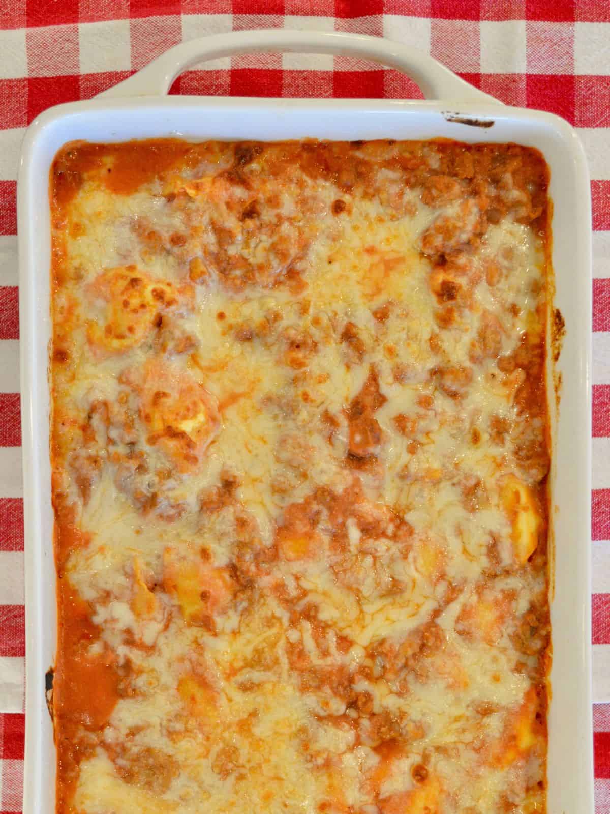 Baked tortellini casserole with a ground turkey meat sauce and ricotta cheese in a white casserole dish. 