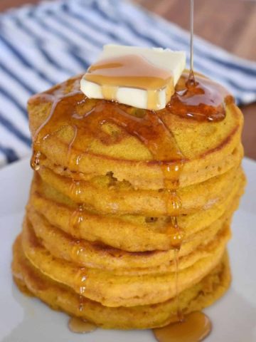 Pumpkin Pancakes with pancake mix on a white plate with maple syrup pouring on top.