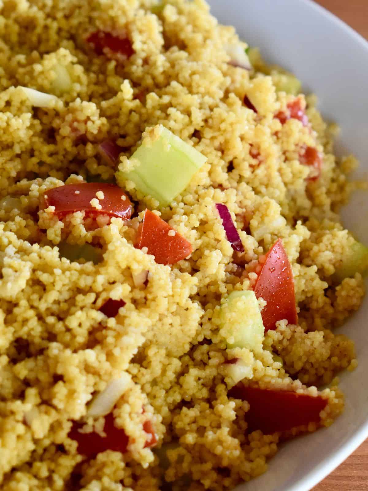 Curried couscous with fresh veggies in a white bowl. 