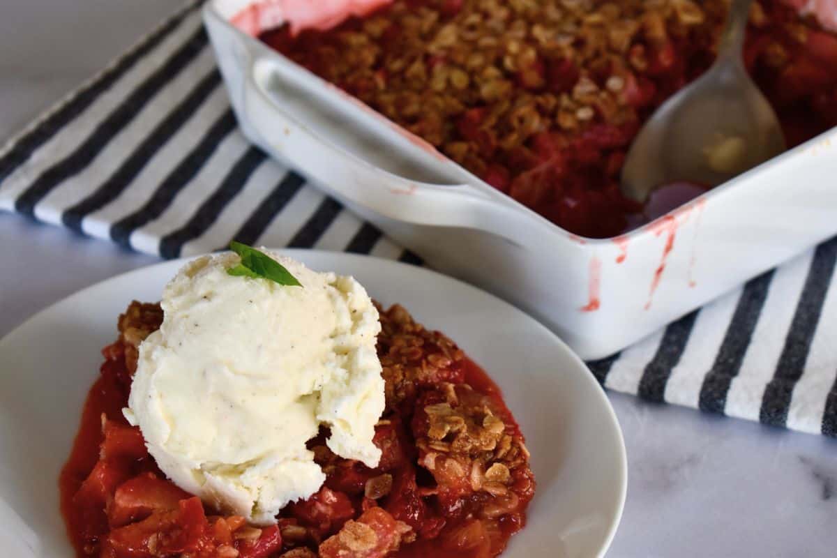Strawberry Rhubarb Crisp on a white plate with ice cream. 