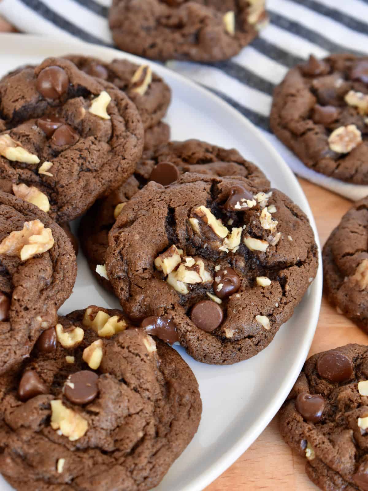 Chocolate Walnut Cookies on a white plate with a striped napkin in the background. 