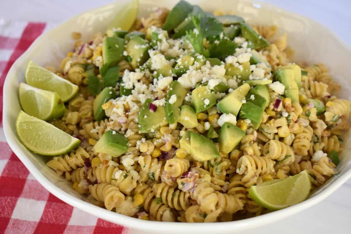 Elote Pasta Salad with avocado and cotija cheese and lime wedges on the side. 