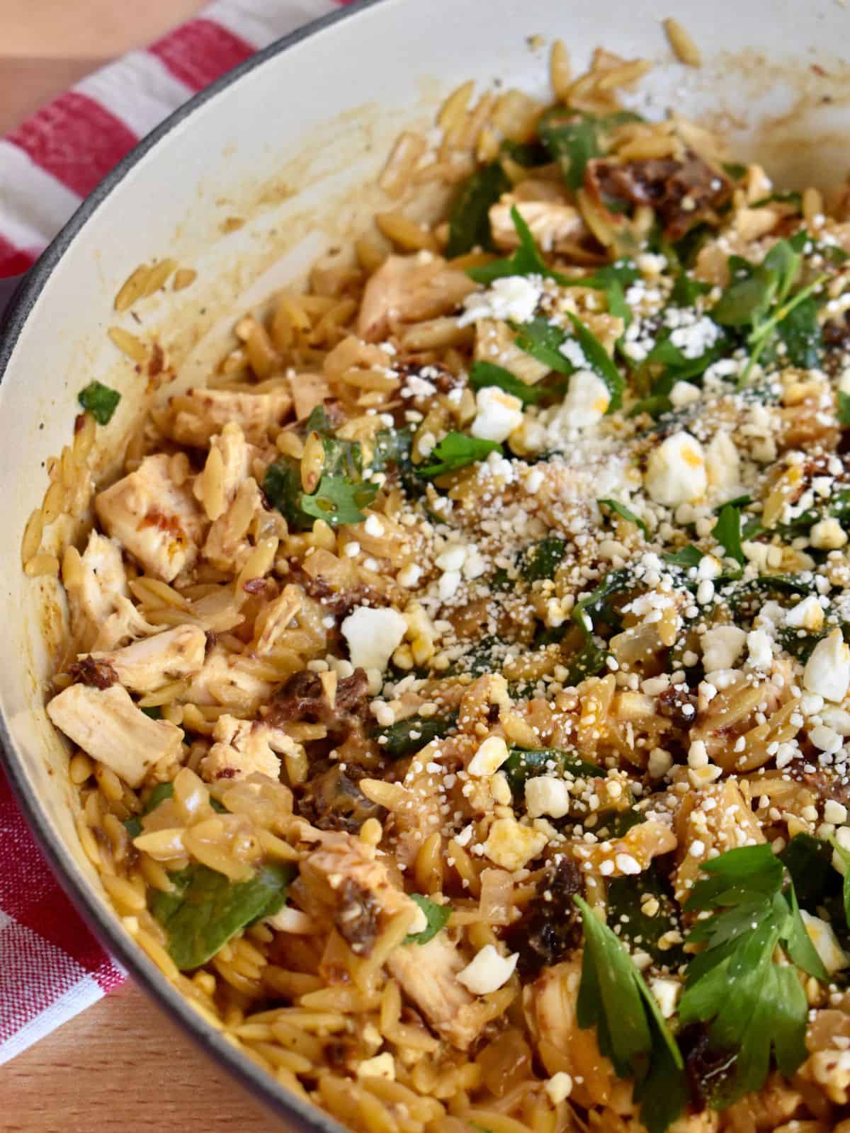 Orzo with Sun Dried Tomatoes and Spinach in a pot with parsley and feta on top. 