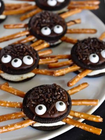 Oreo Cookie Spiders with pretzel legs on a white plate.