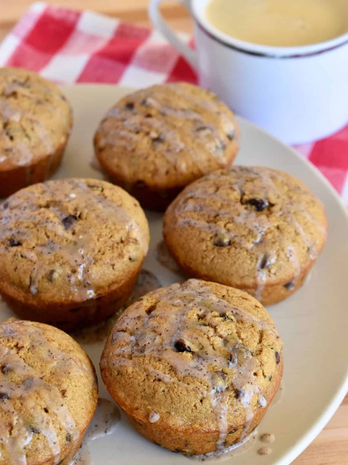 Cappuccino Muffins with easy espresso glaze on a plate with a cup of coffee next to it. 