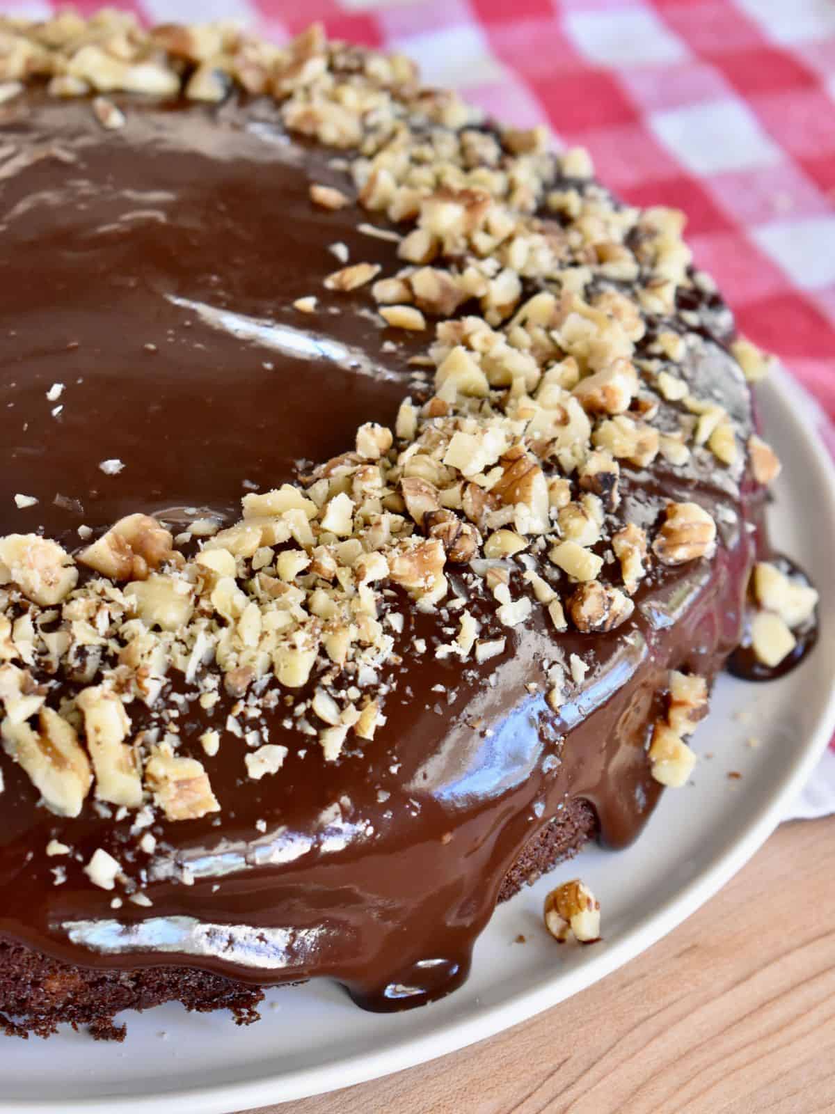 Chocolate Walnut cake with chocolate ganache frosting on a white plate with chopped walnuts on top. 