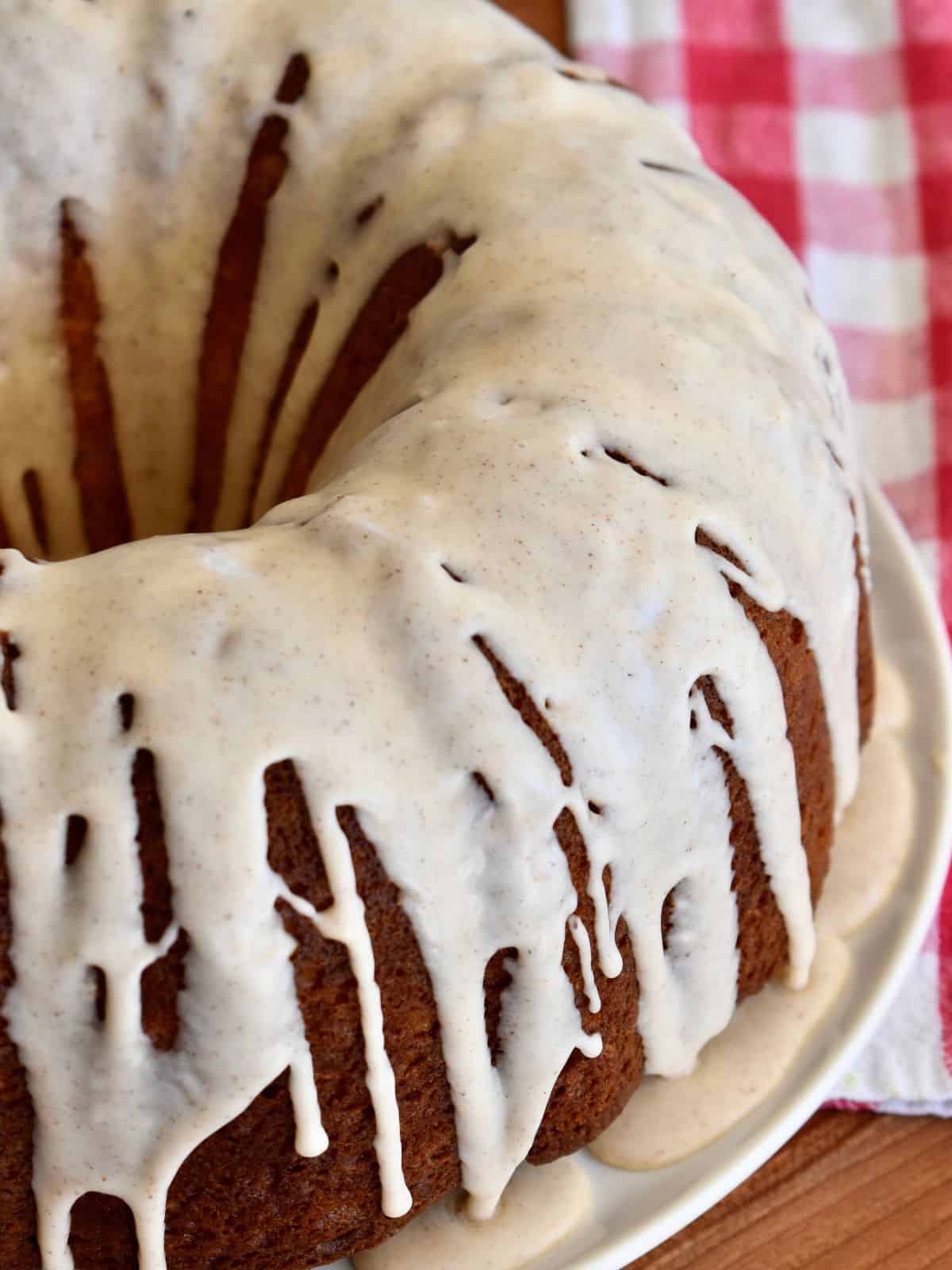Eggnog Bundt Cake with eggnog glaze on a white plate with a checkered napkin in the background. 