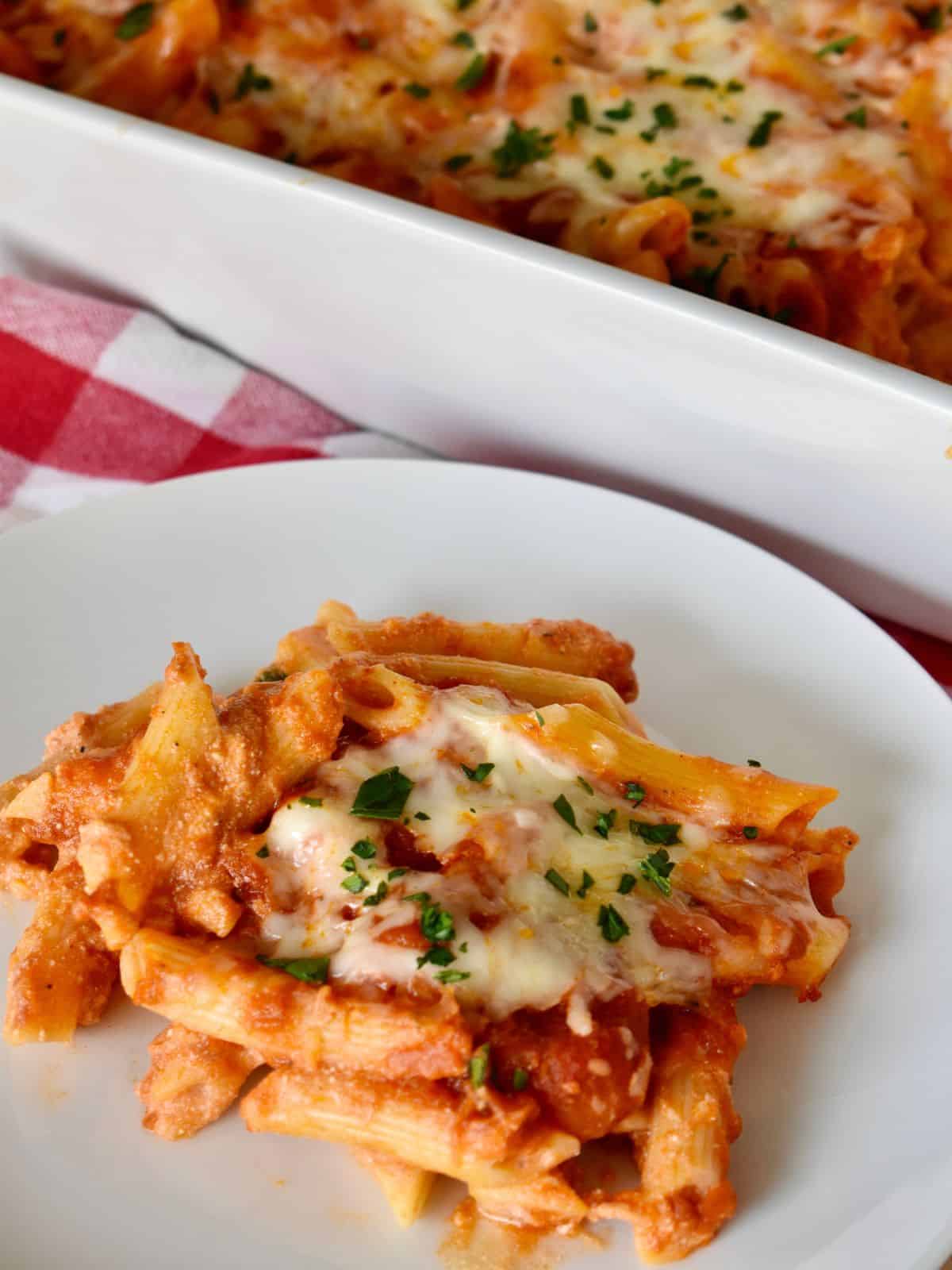 Baked penne with ricotta on a white plate with a casserole dish in the background. 