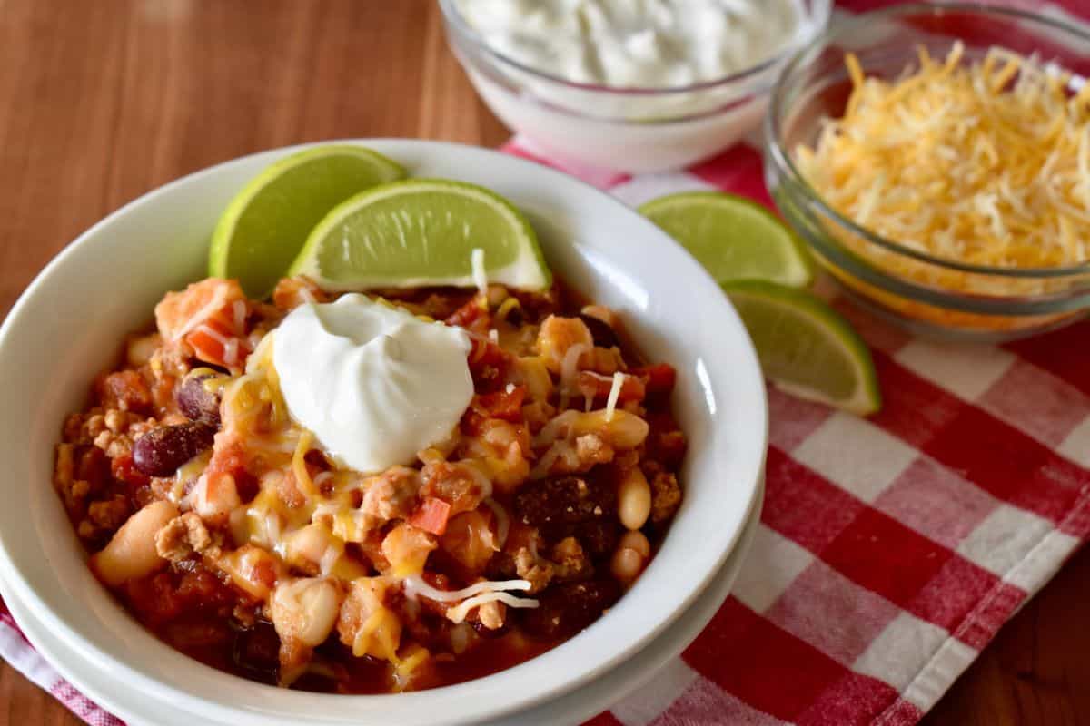 Turkey Chili with hominy in a white bowl topped with sour cream. 