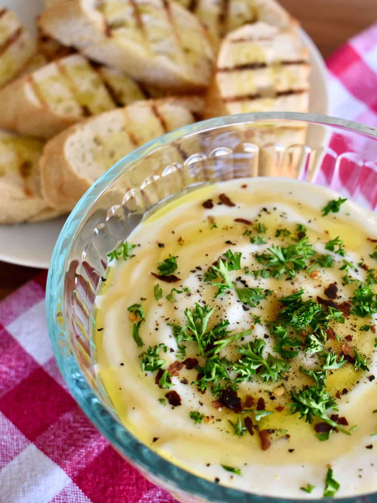 Whipped ricotta dip in a glass bowl with grilled baguettes. 