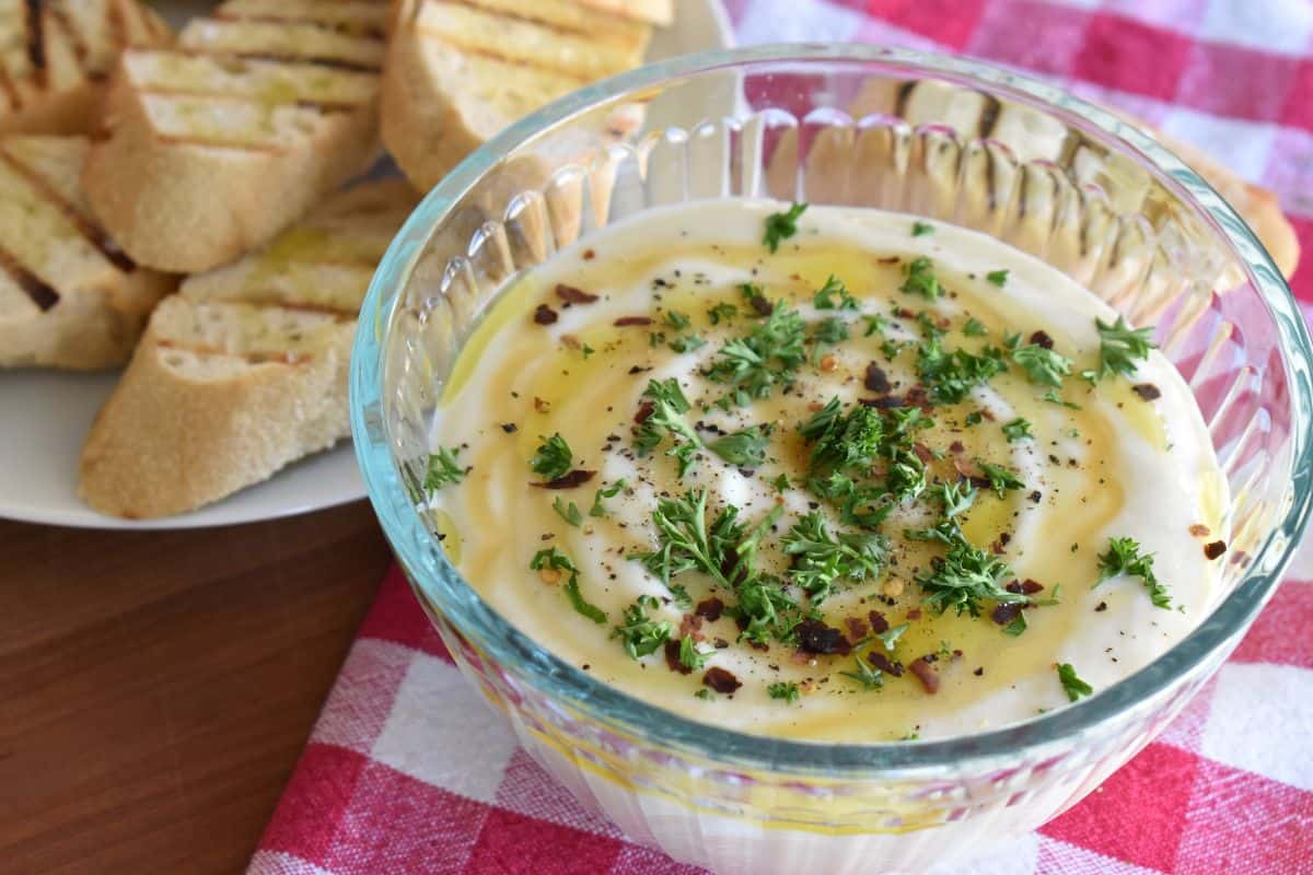 Whipped Ricotta Dip in a glass bowl with garnishes and grilled bread served next to it. 