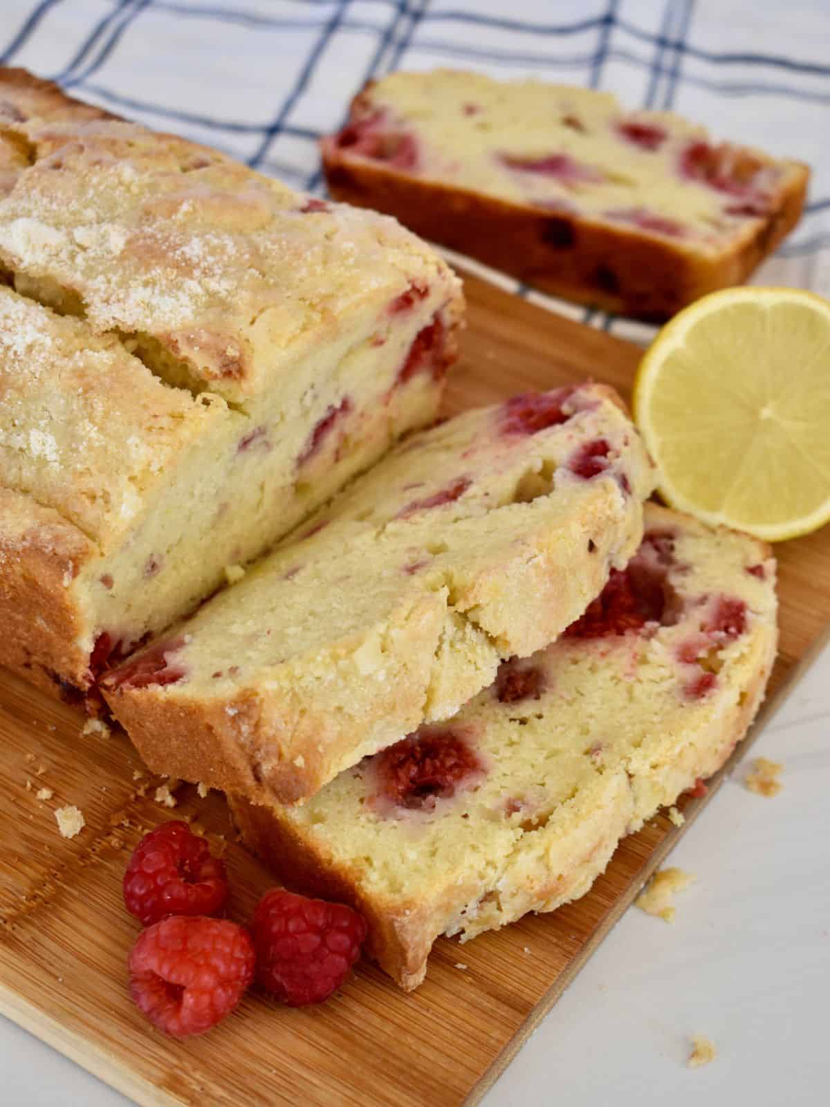 Lemon raspberry loaf cake on a cutting board with raspberries and lemon next to it. 