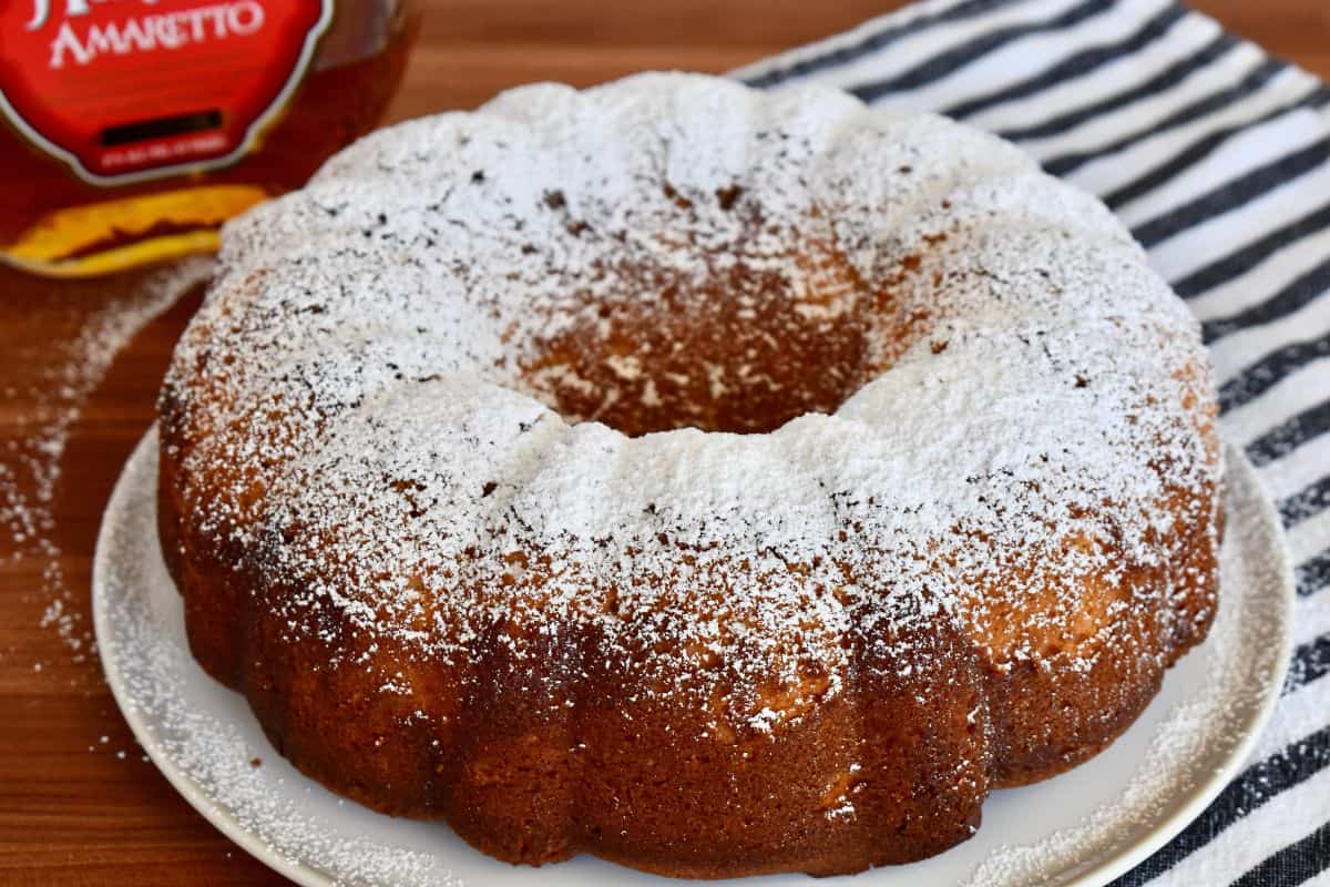 Amaretto pound cake on a white plate with powdered sugar sprinkled on top. 