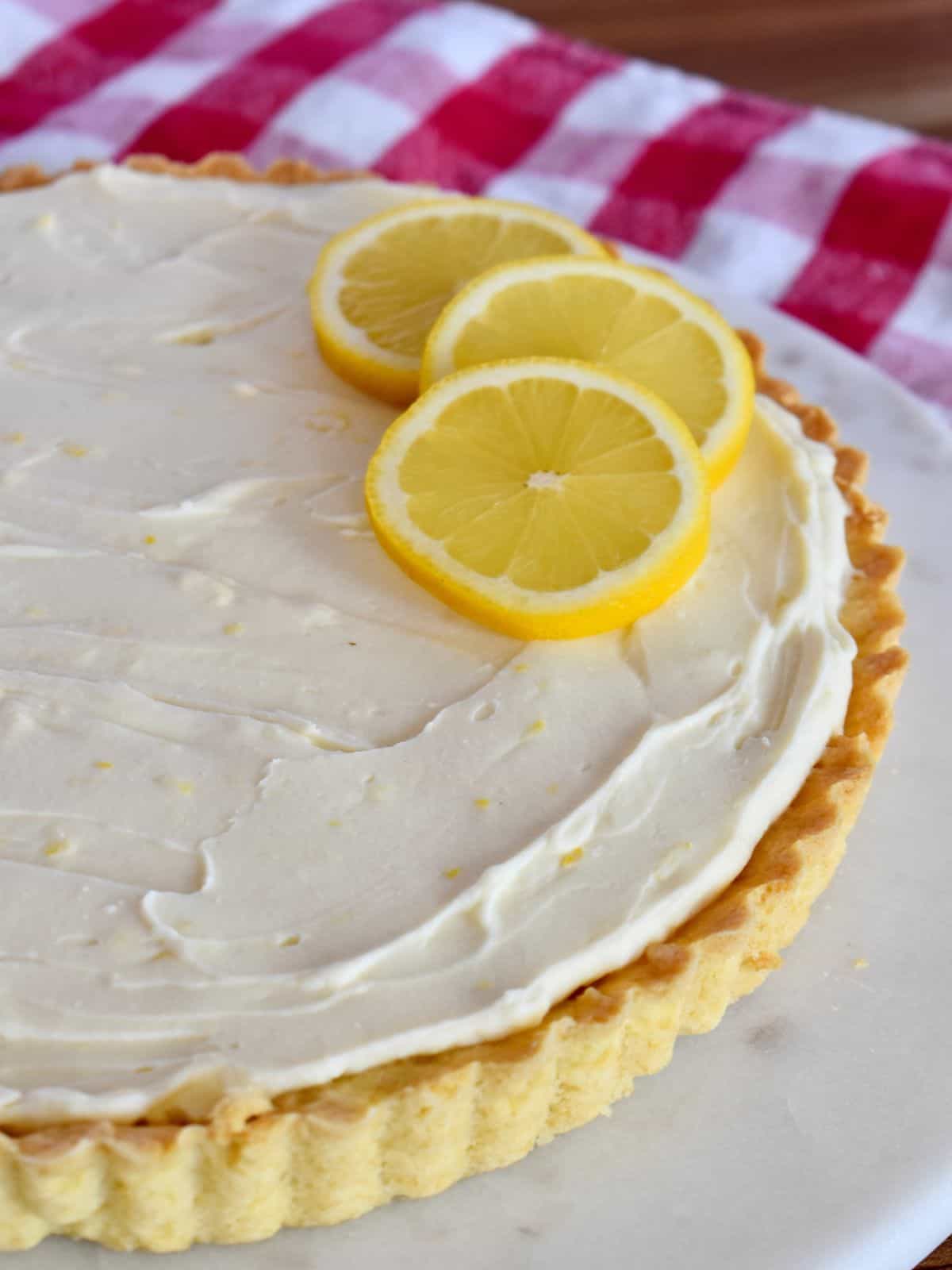 Lemon Mascarpone Tart on a white serving platter with a checkered napkin in the background. 