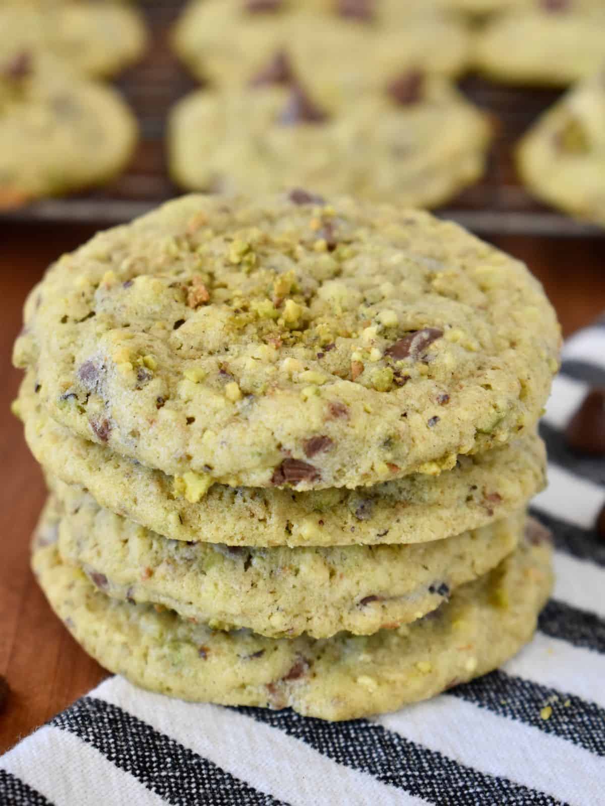 Chocolate Chip Pistachio Cookies stacked with a wire rack of cookies in the background. 