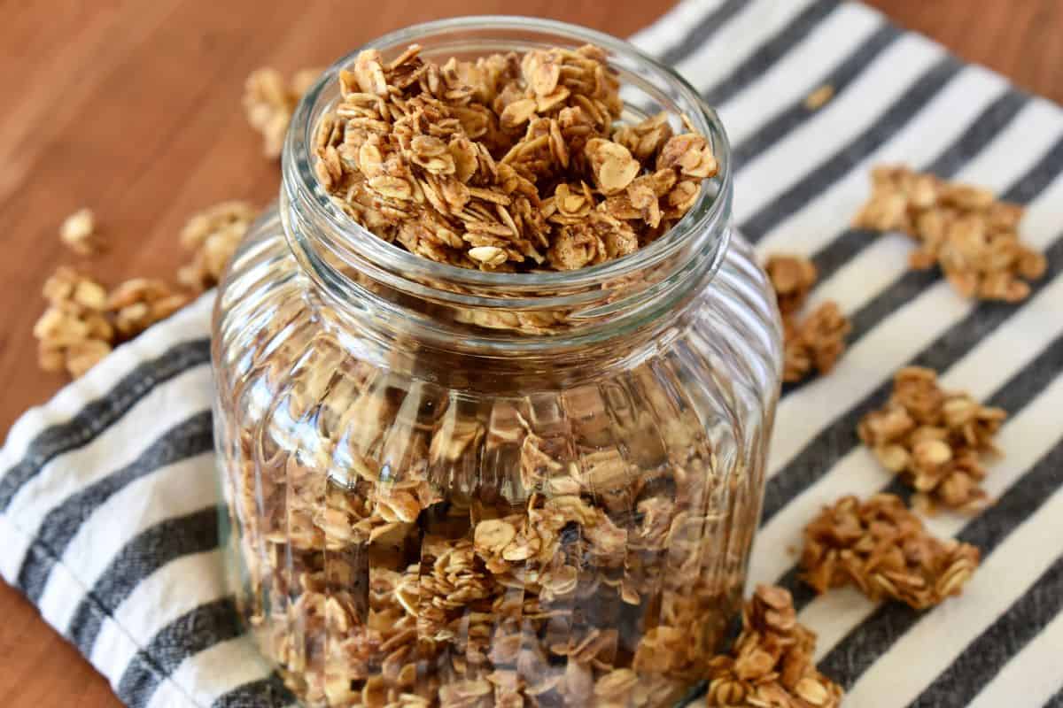 Granola Recipe without Nuts in a glass container on a countertop on striped napkin. 