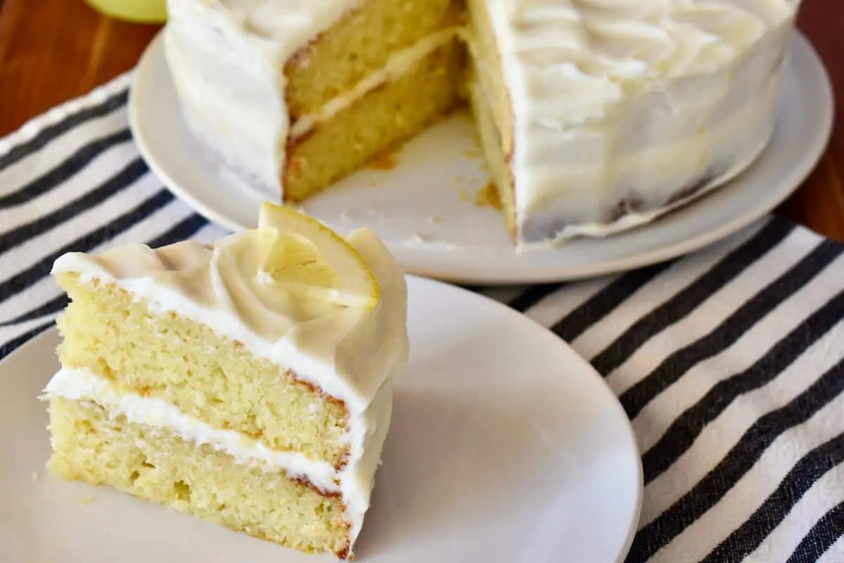 Slice of limoncello ricotta cake on a plate with the cake in the background. 