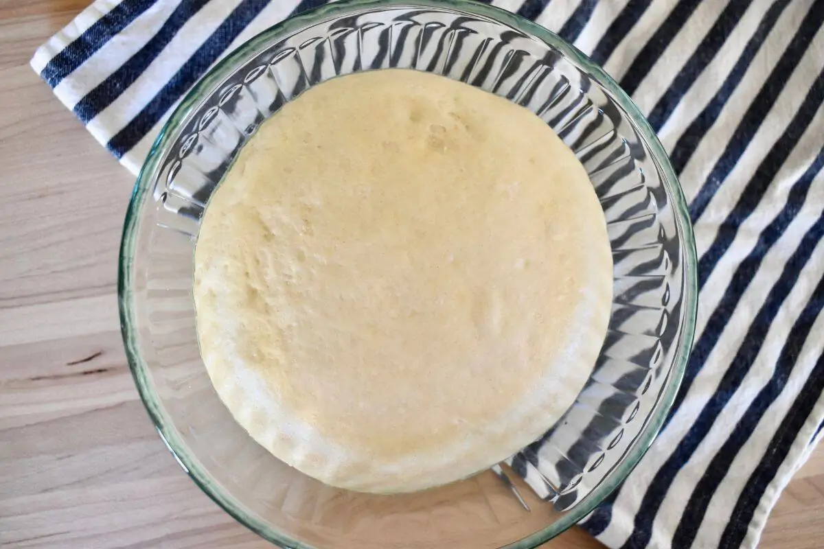 Small batch pizza dough in a glass mixing bowl on top of a striped napkin. 