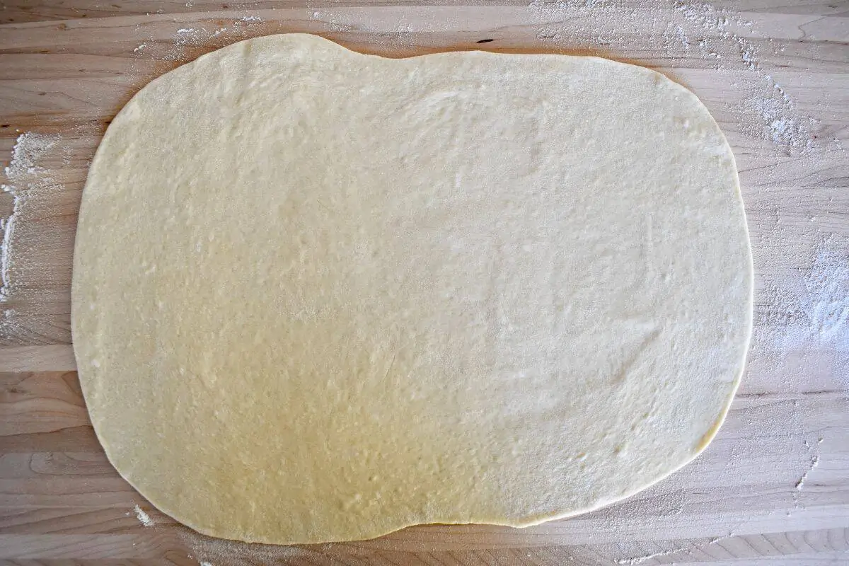 Small batch pizza dough rolled into a rectangular shape on a wood cutting board. 