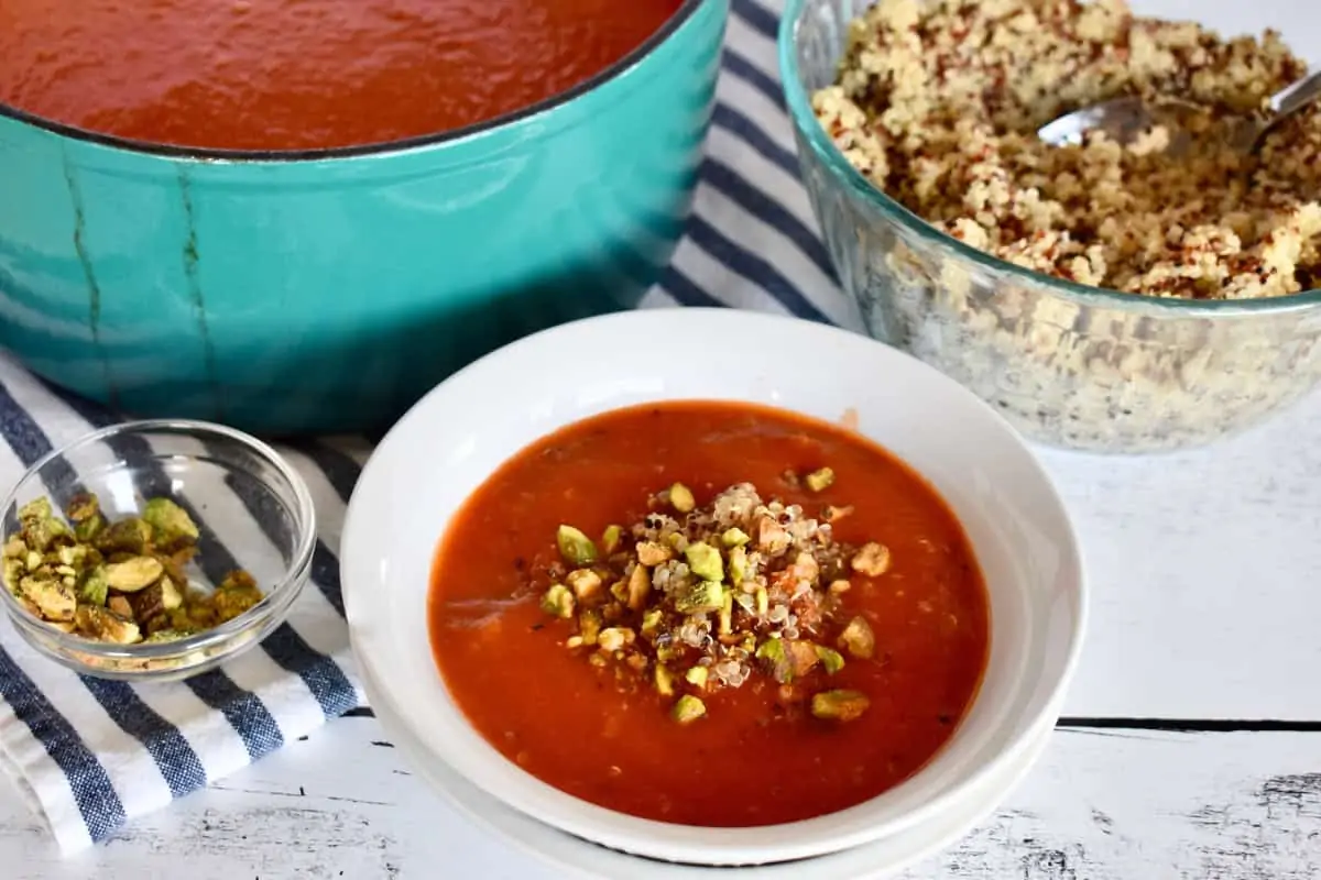 Tomato Quinoa Soup in a white bowl with chopped pistachios on top. 