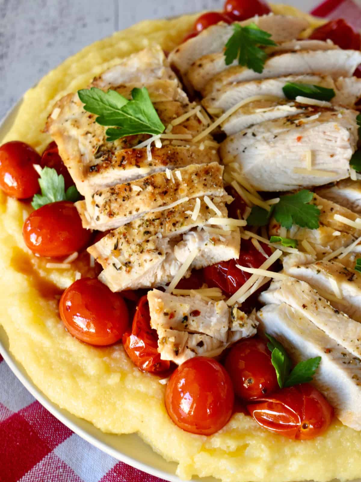 Large plate with polenta, chicken and cherry tomatoes, topped with parmesan cheese. 