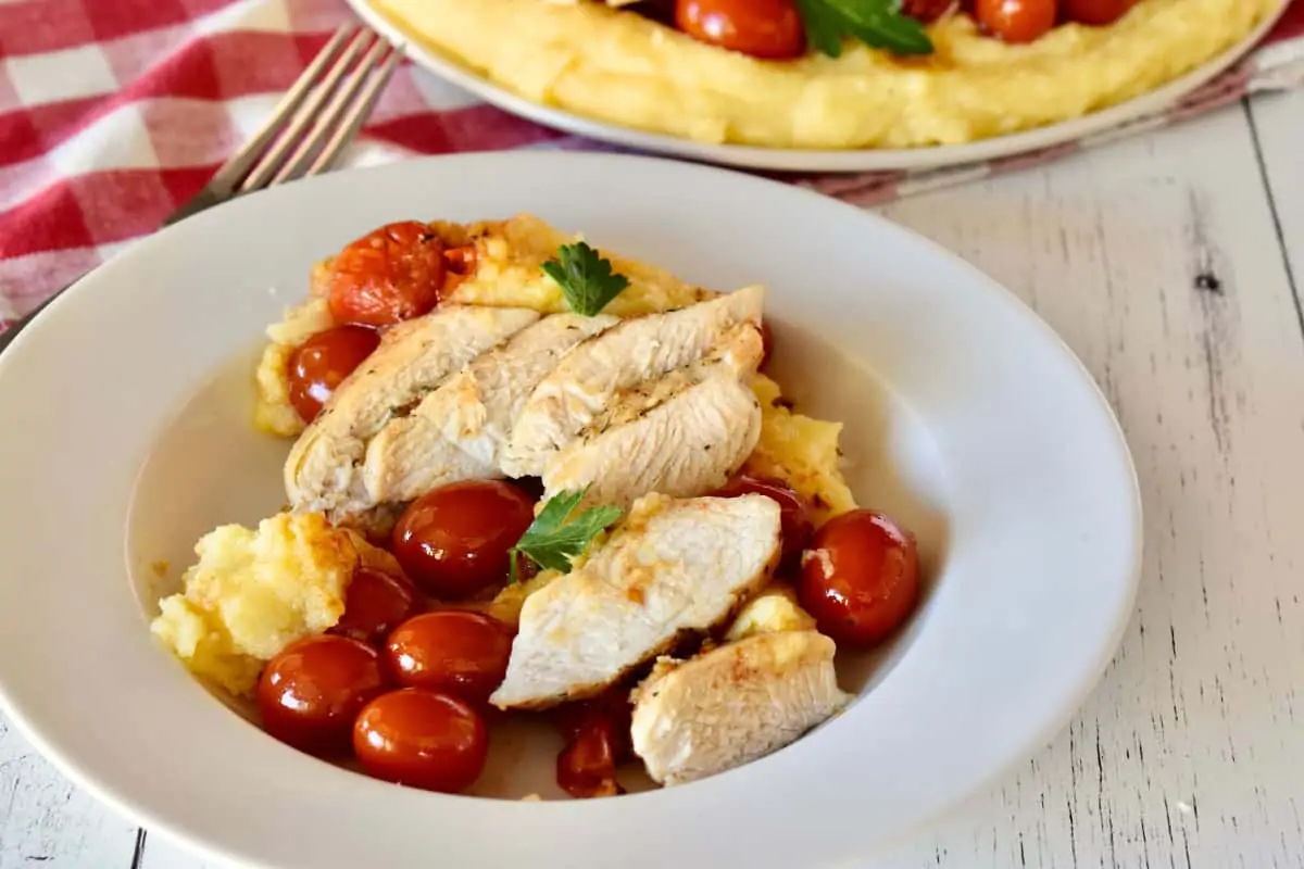 Chicken with polenta in a white bowl with cherry tomatoes. 