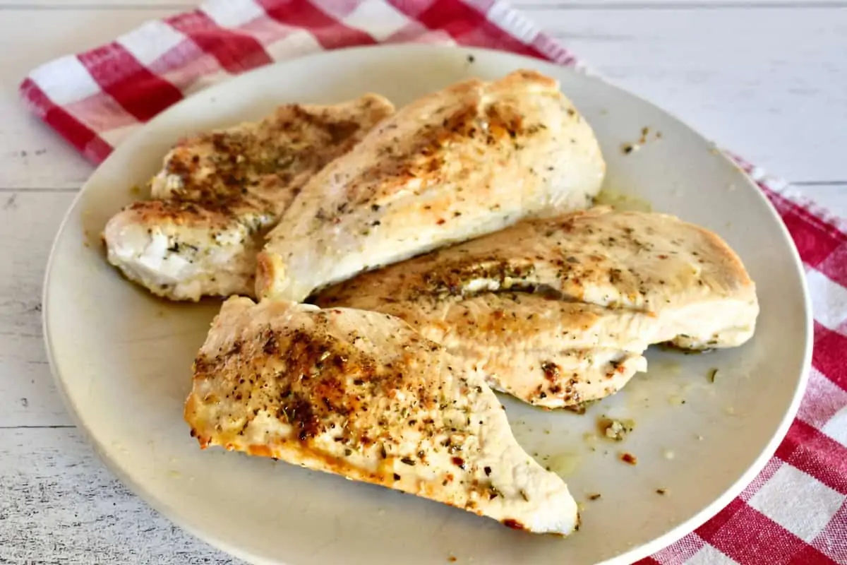 Cooked chicken breasts on a plate with a checkered napkin underneath. 