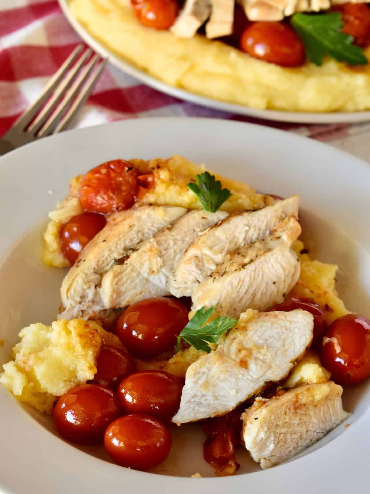 Chicken with Polenta and cherry tomatoes in a white bowl. 