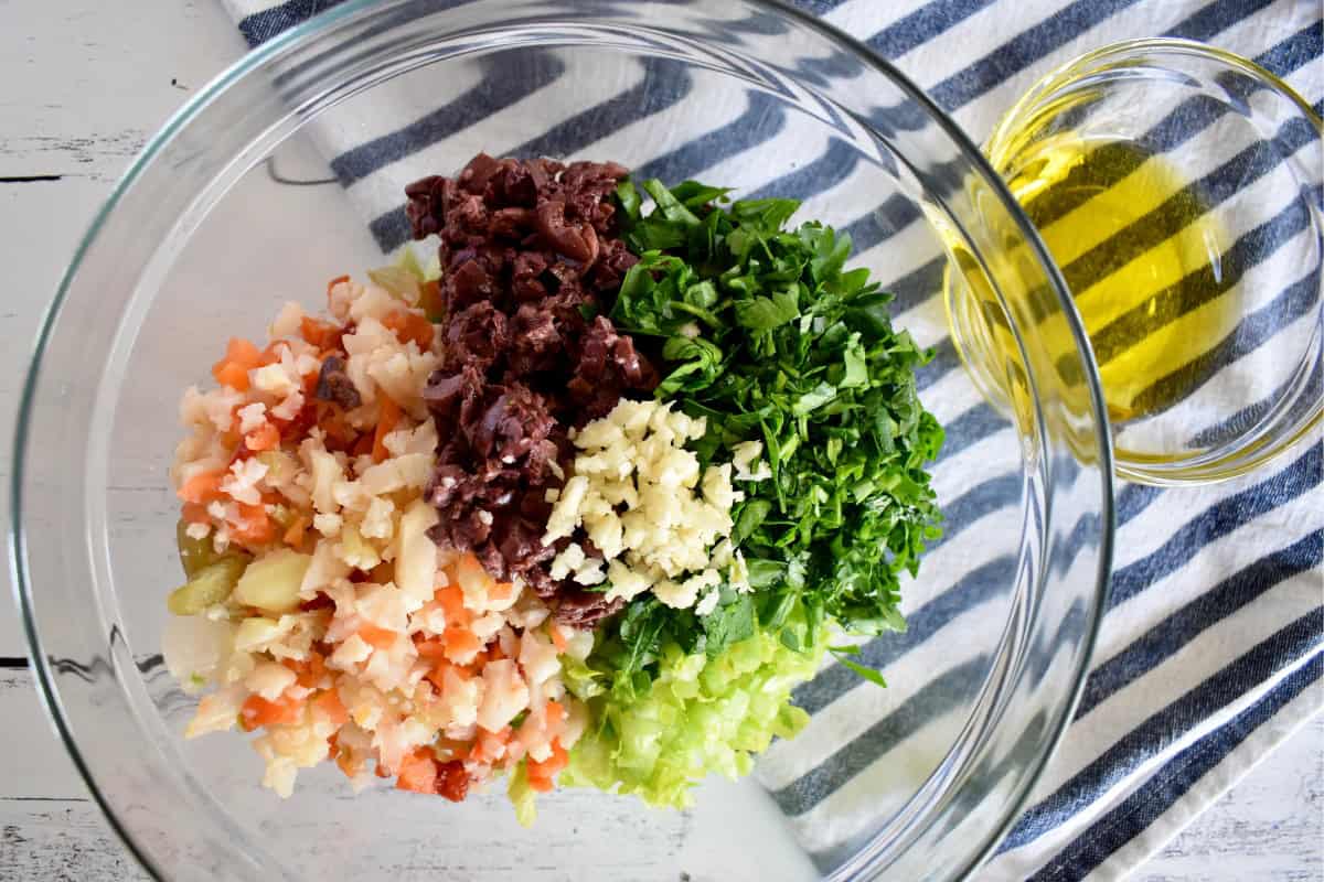 Chopped olives, giardiniera, celery, garlic, and parsley in a glass bowl. 