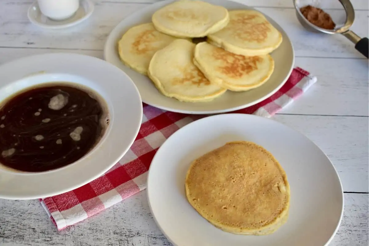 Pancake on a white plate with a bowl of warm espresso next to it. 