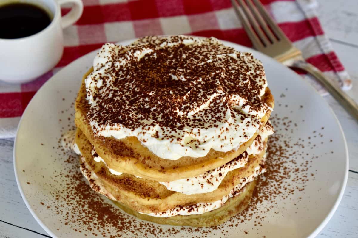 Stack of tiramisu pancakes on a white plate with cocoa powder sprinkled on top. 