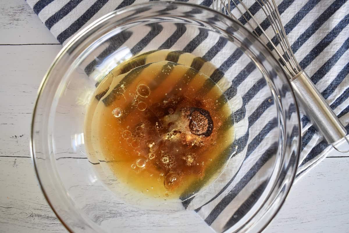 Honey, oil, water, and other wet ingredients mixed in a glass bowl.