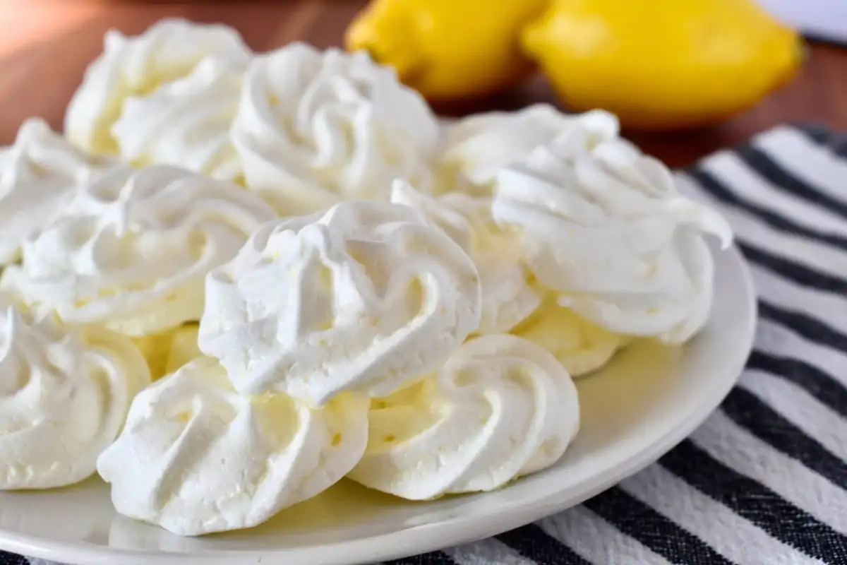 Lemon Meringue cookies on a white plate with lemons in the background.