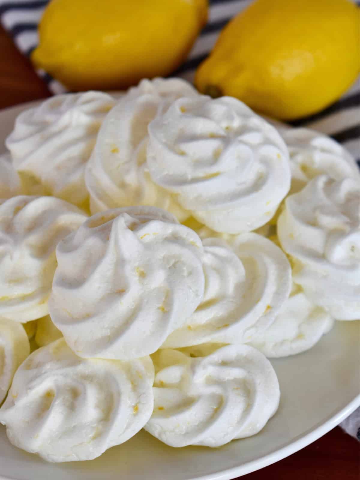 Lemon meringue cookies on a white plate with lemons in the background.