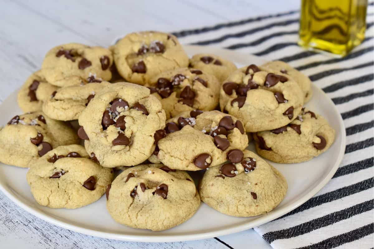 Olive oil chocolate chip cookies on a plate with a bottle of olive oil in the background.
