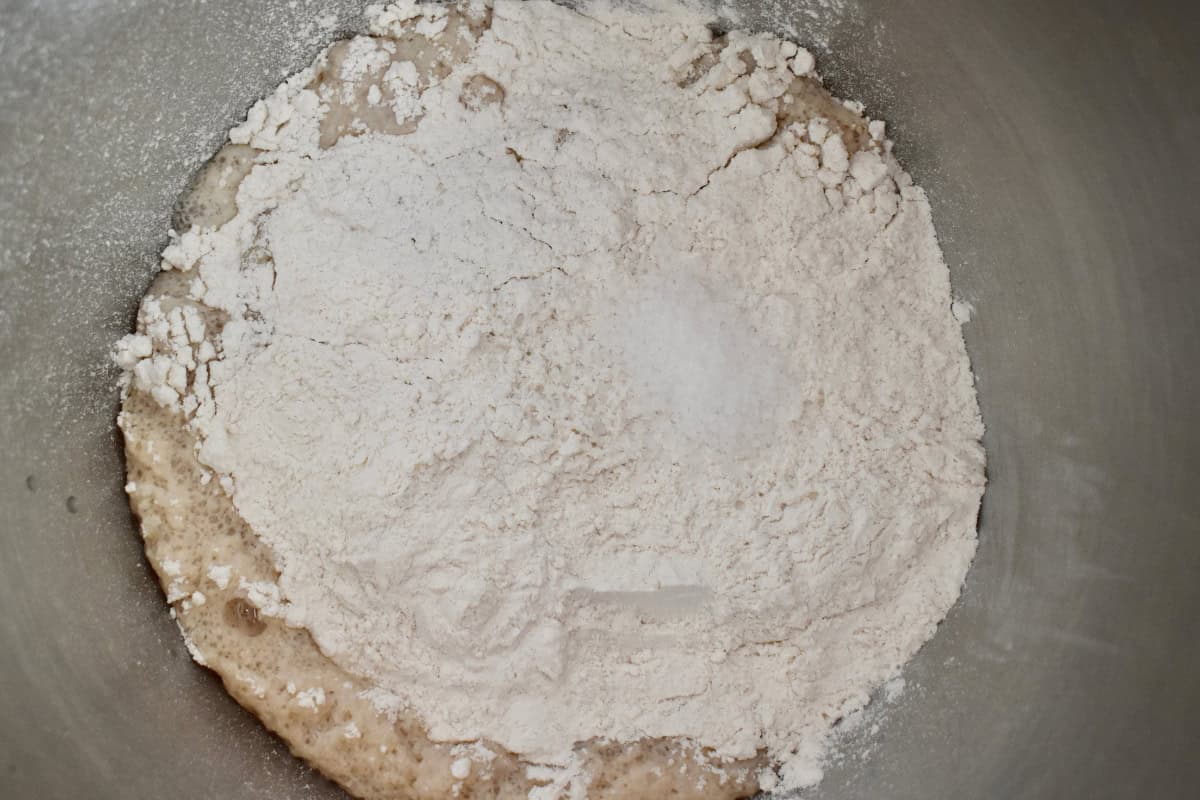 Flour added to the yeast mixture in a large metal bowl. 