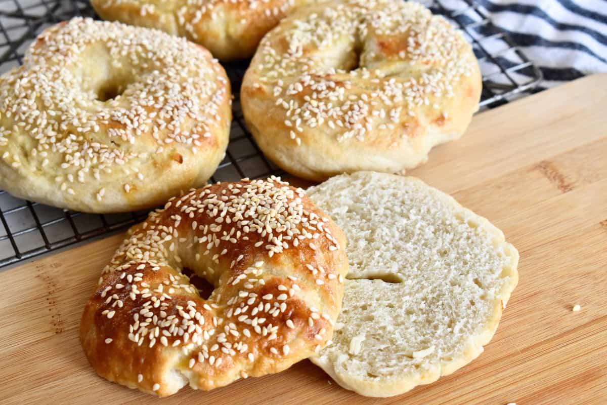 Sesame Seed Bagels on a cutting board with one sliced in half. 