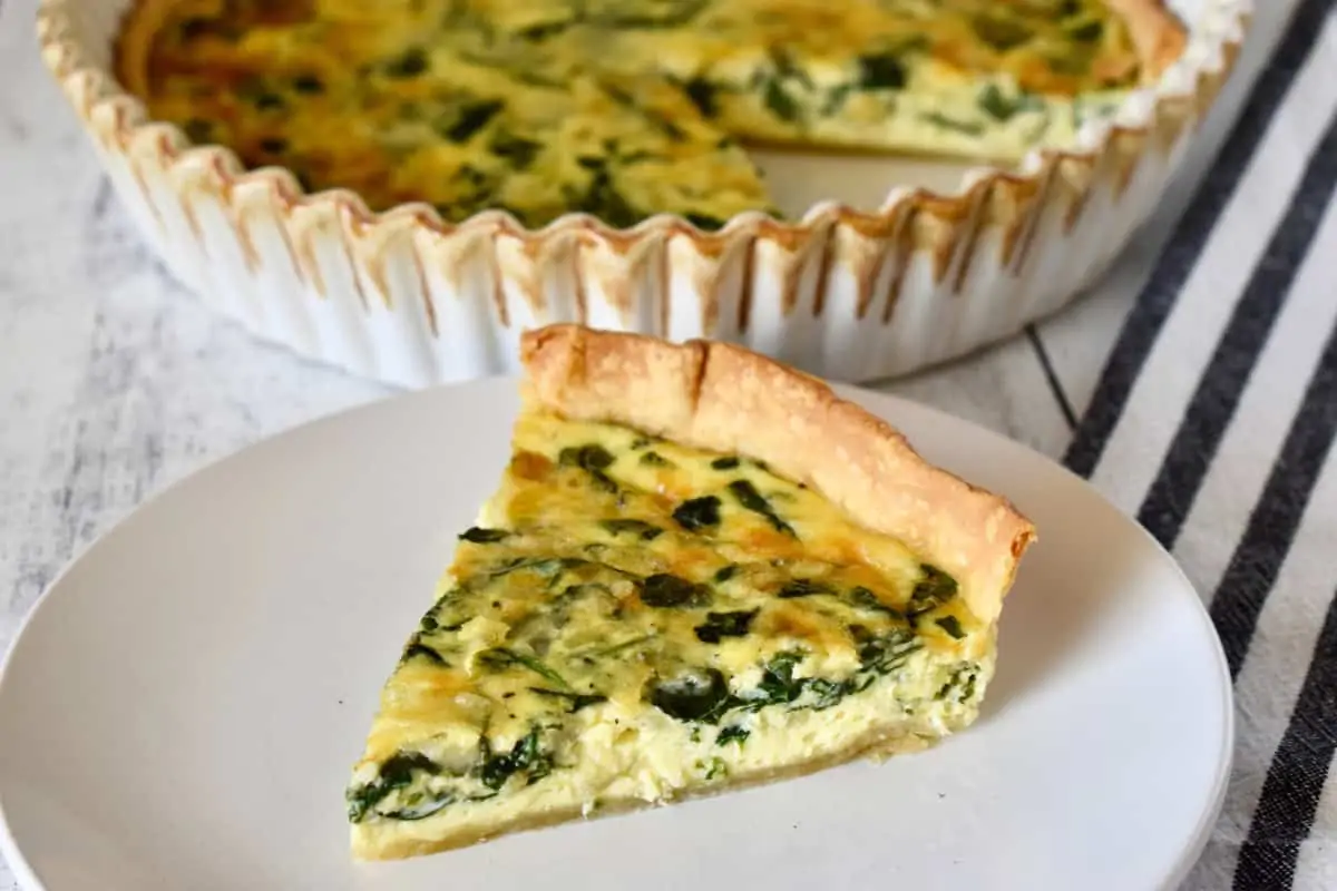Slice of spinach gruyere quiche with store bought crust on a white plate. 