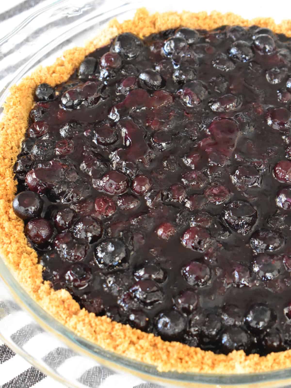 Blueberry pie with graham cracker crust in a glass pie pan. 