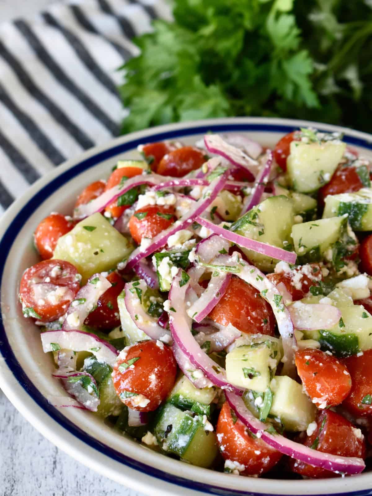 Cucumber Tomato feta salad in bowl on a checkered napkin with parsley.