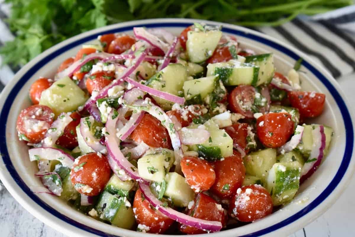 Cucumber Tomato Feta salad in a white bowl with red onions in it.