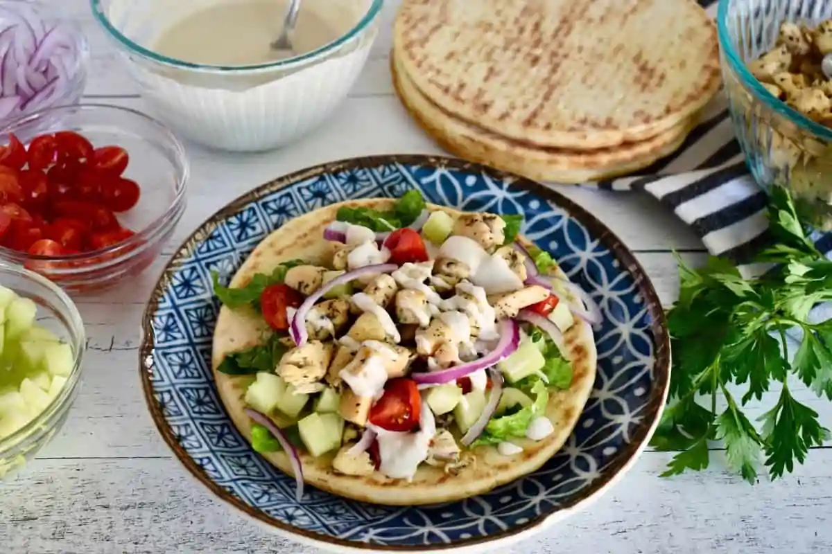 Pita on a plate with chicken and veggies and tahini sauce on top.