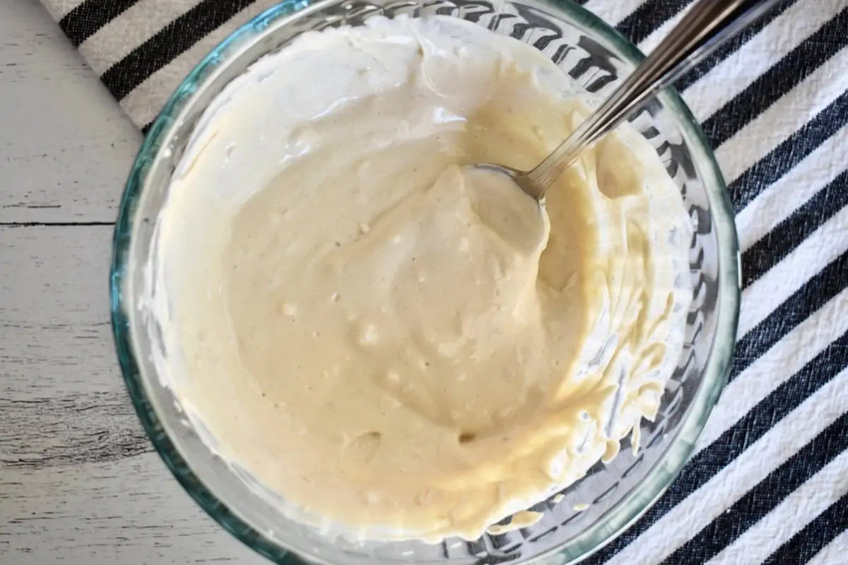 Tahini sauce in a glass bowl with a spoon.